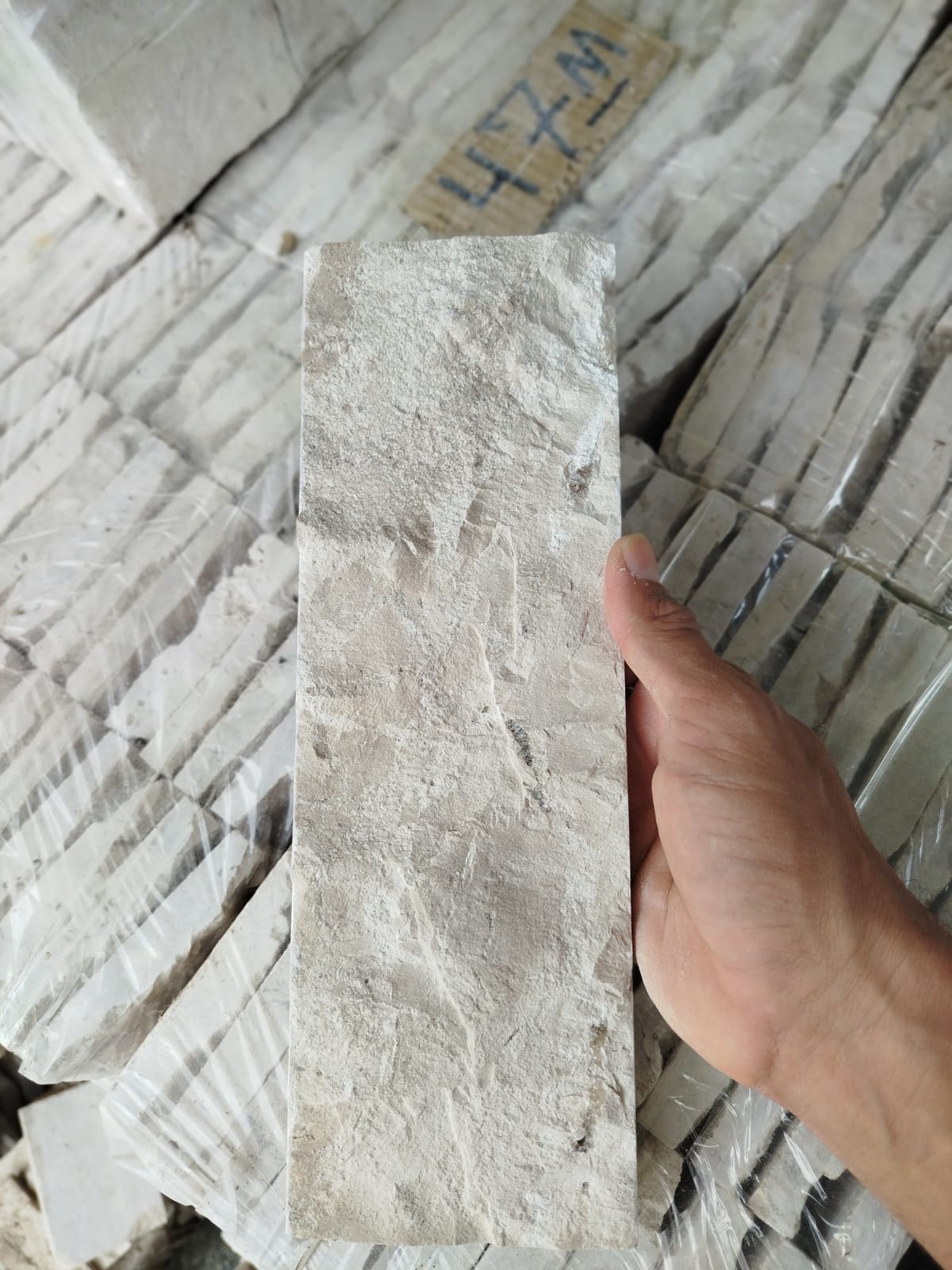 Peça de Rockface em Travertino Nacional segurada na mão para mostrar a escala